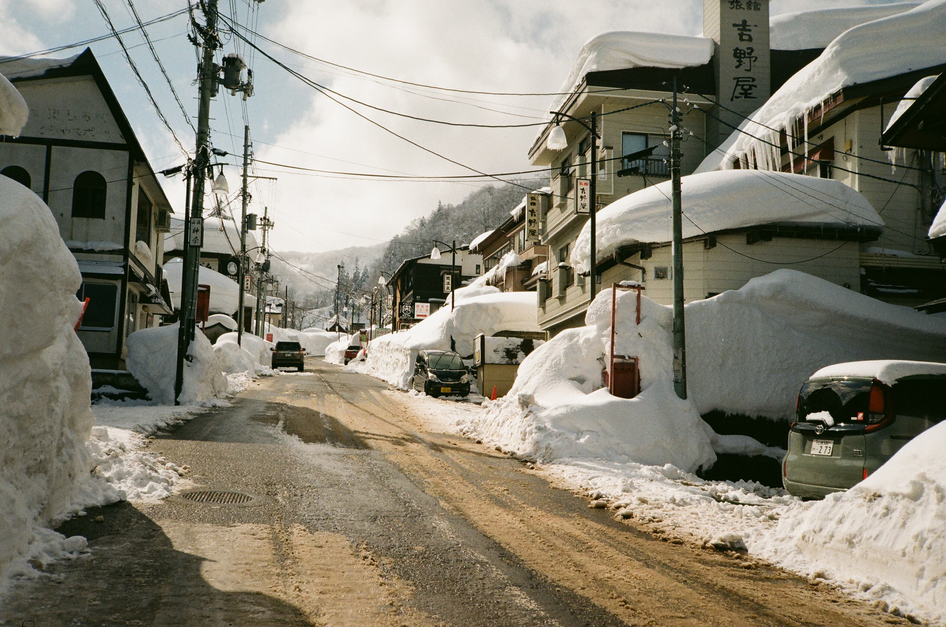 Snow-buried village street with ryokan signage in Honshu Japan, photo by Kinman Bailey